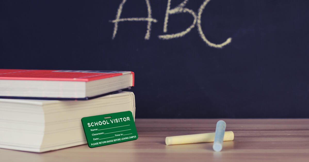 Books, Visitor Name Tag, and Chalk on a Desk in Front of a Blackboard with "ABC" Written in Chalk